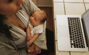 Mother using a computer while holding her sleeping baby