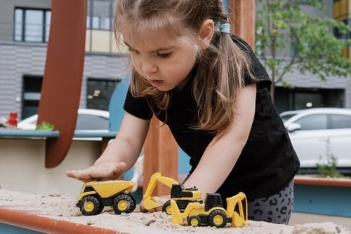 Focused little girl playing with toy construction trucks in the sand