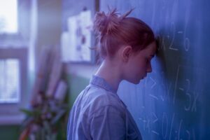 frustrated, hopeless teenage girl standing with forehead against a blackboard of algebraic equations