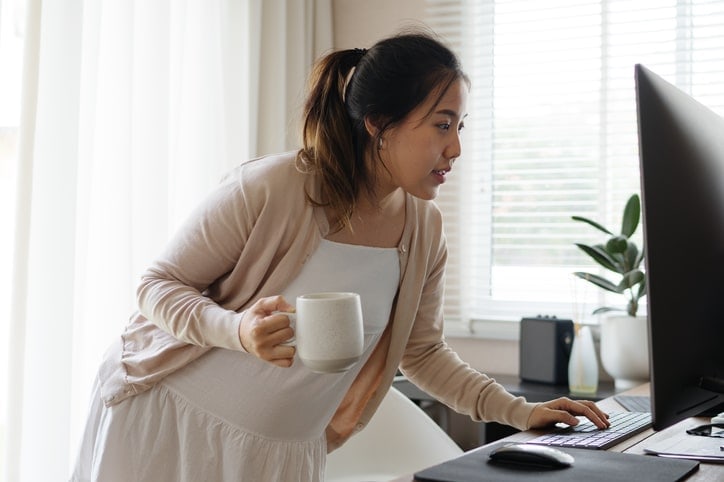 woman looking at computer while holding a coffee mug