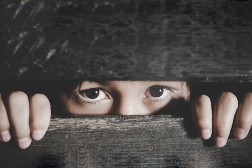 child's worried eyes peering through an opening in a wooden fence
