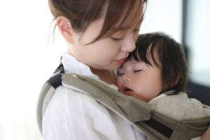attachment parenting - mother holding sleeping infant in sling on her chest