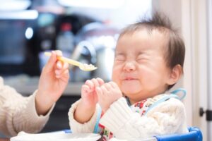 infant screwing up face and closing eyes in response to food being offered on a spoon