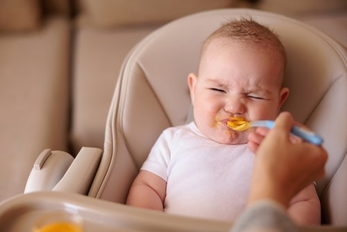 infant squints and scowls while tasting pumpkin puree from a spoon