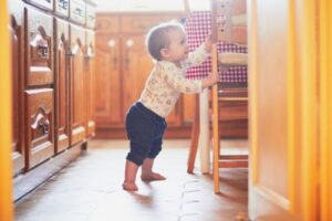baby pulling herself into standing position by grapsing chair in the kitchen