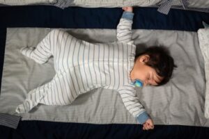 older infant sleeping in cot, arms outstretched