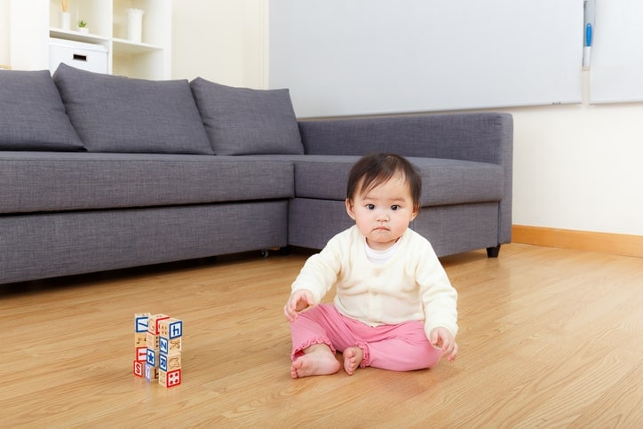 baby sitting on wooden floor, both arms outstretched in air
