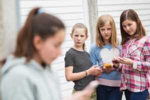 playground primary school scene - three girl bullies looking up from their phones and sneering at a fourth girl