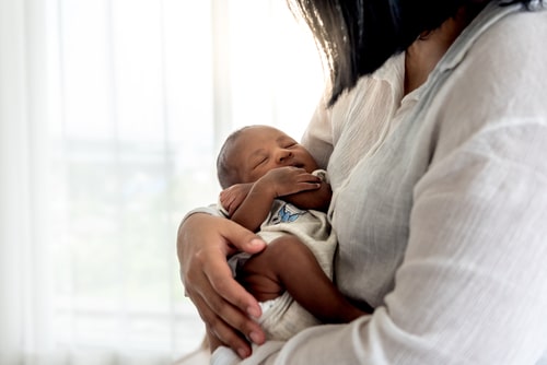 sleeping newborn infant with folded arms, being carried by mother