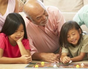 family playing a board game - grandfather leaning on the floor with two grandchildren