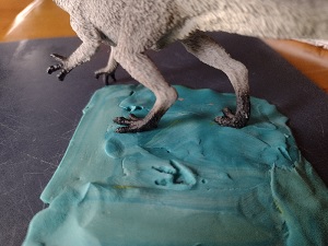 toy dinosaur feet being pressed into clay and leaving tracks