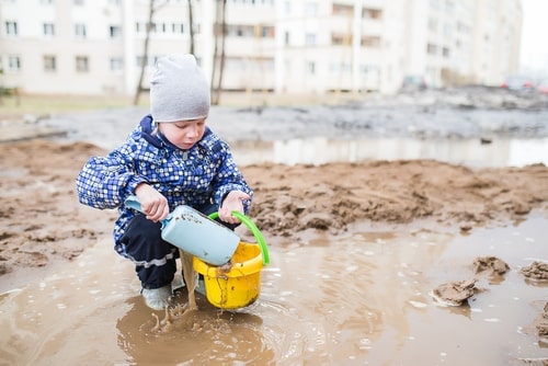 boy outdoors, engaged in a dirt lab, shoveling mud into bucket