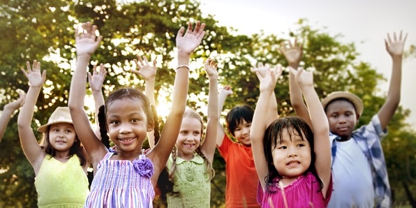 kids of different races cheerfully raising their hands against a backdrop of trees