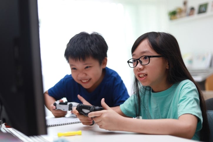 two kids playing video game at a desk, looking happy and intense
