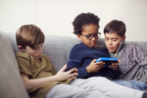 three boys relaxing on couch, playing video games on handheld devices