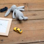 child's stuffed toy and cars left abandoned on worn wooden floor, next to a broken picture frame