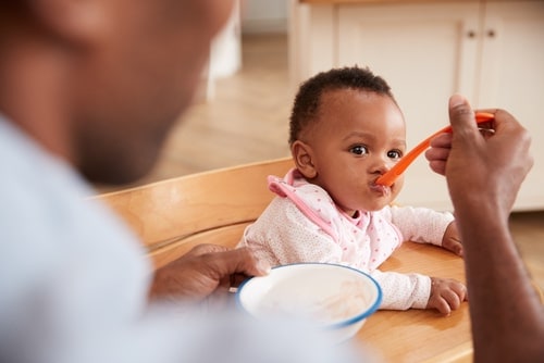 baby at high chair, father spoon feeding infant cereal 