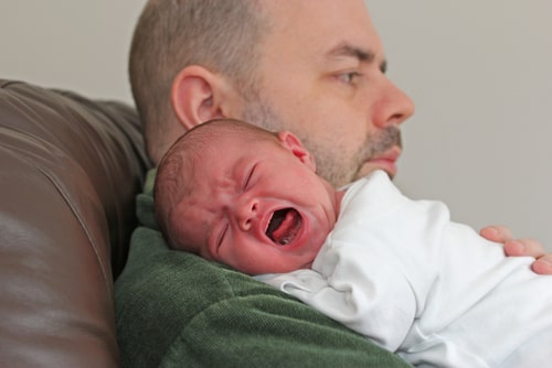 tired,calm father holds red faced, crying, screaming baby over his shoulder