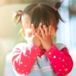 frustrated toddler girl covers face with her hands
