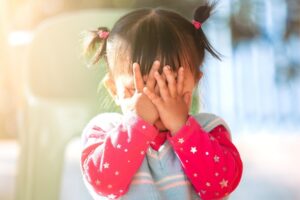 frustrated toddler girl covers face with her hands