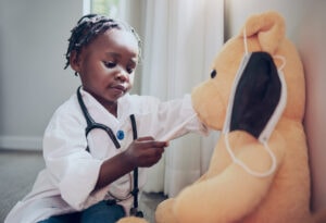 little girl pretending to be a doctor while examining her teddybear at home