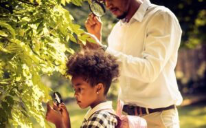 little girl with father, looking intently through a magnifying glass at the leaves on a bush