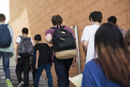 high school students, viewed from behind as they ascend the stairs to school