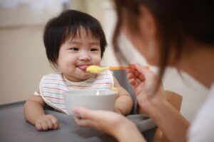 cute baby sticks tongue out in anticipation of mother's spoon feeding