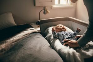 mother putting baby to bed in "sleep side car" alongside mother's bed