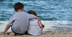 young children sitting on the beach, boy is consoling little girl