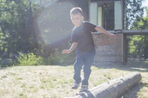 boy dislaying gross motor skills, balancing on one leg while he walks on a log