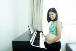 pregnant woman holds her belly, thoughtfully, while playing the piano