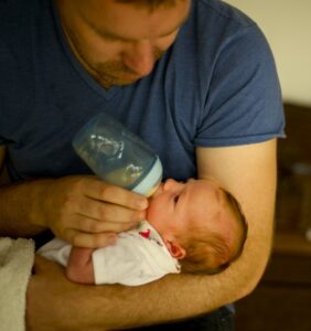 father breastfeeding with baby bottle her little new born daughter