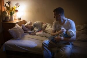 father feeding newborn at night while mother sleeps