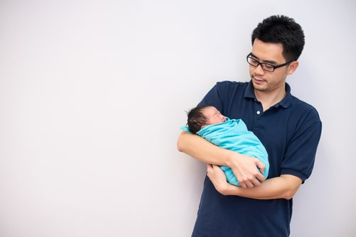 father looks quizzically at newborn bundled in his arms