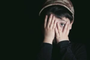 Young boy covering face, one eye peeking out, fearful manner
