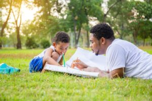 father and son drawing pictures together on the grass in a park