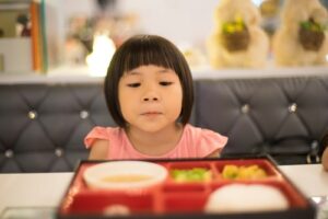 Young girl peers into bento box, eyeing vegetables with wariness