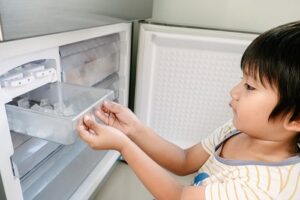 preschool boy carefully removing ice tray from freezer