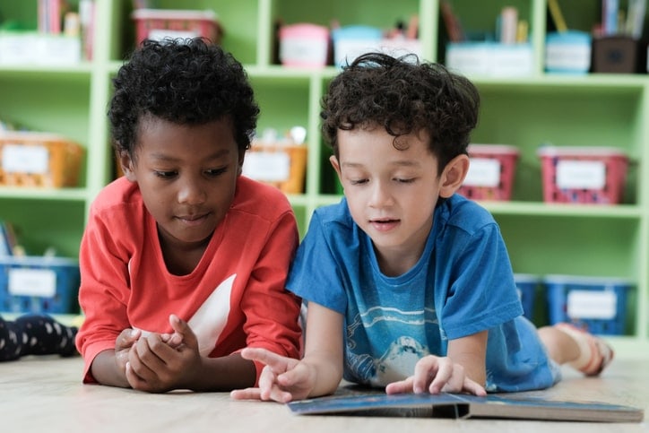 two young boys sitting on floor reading a book together