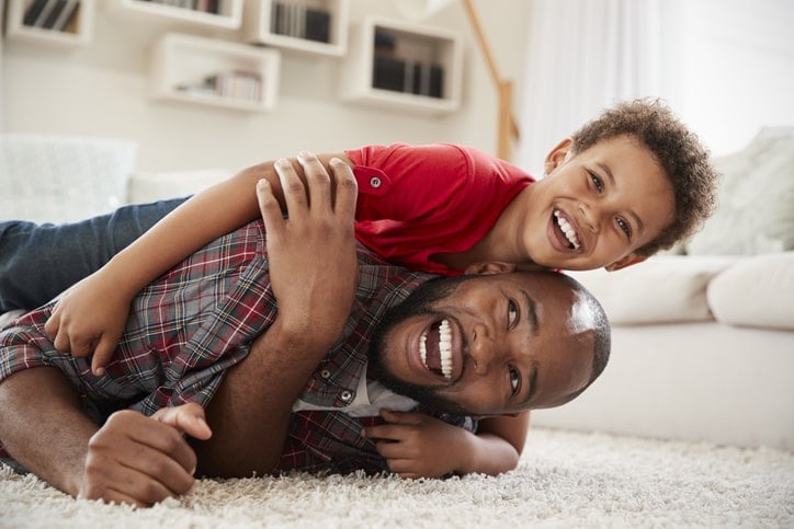 father and son laughing and tumbling on the floor, boy is on top
