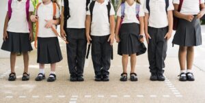 young children wearing school uniforms, with girls in skirts and mary janes, and boys in trousers and lace-up shoes