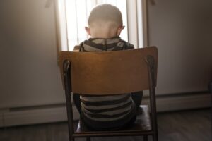 downcast boy sitting in chair with back to viewer