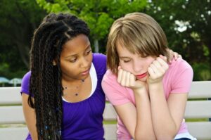 two teenage girls - one looking upset and the other showing empathy and kindness