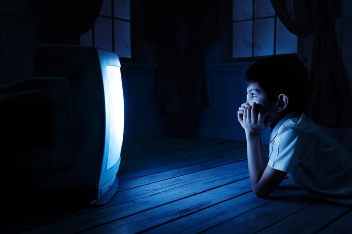 young boy on the floor, in the dark, watching television