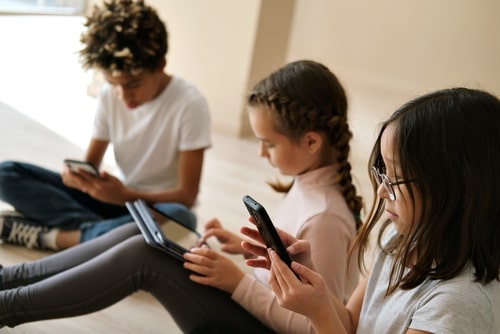 three kids sitting on the floor, each in the grip of a video game addiction, each playing on their own device