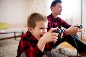 joyful, preschool-aged boy playing video games with father