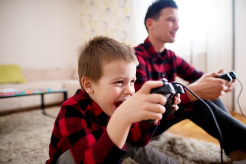intense and happy young boy playing video game with father