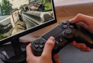 closeup of hand operating video game controller and first person shooter game on screen