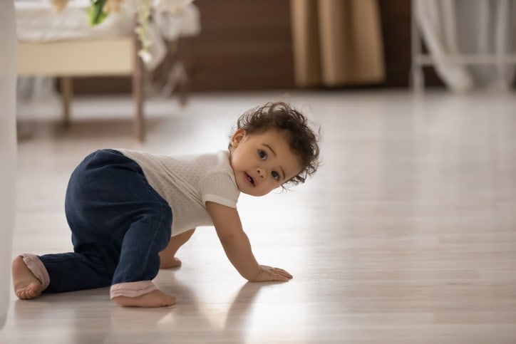 infant looks over shoulder while crawling on hands and one knee